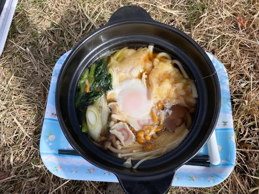 草むらの上にお盆と鍋焼きうどん